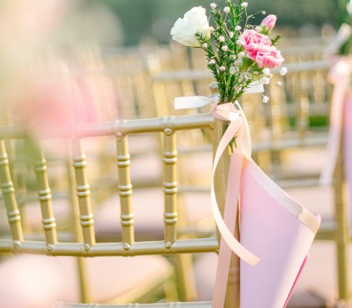 Gold chairs with ribbons and flowers set out for a ceremony