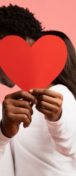 A person holding a red paper heart in front of their face