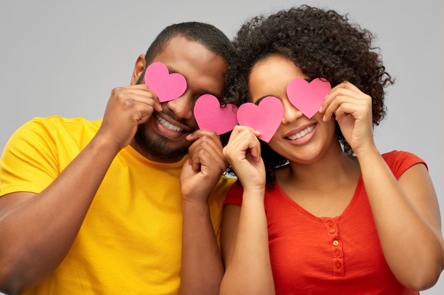Couple holding pink paper hearts over their eyes